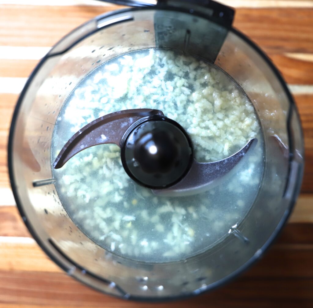 Place the garlic and lemon juice into the food processor and let it sit for about 5 minutes.